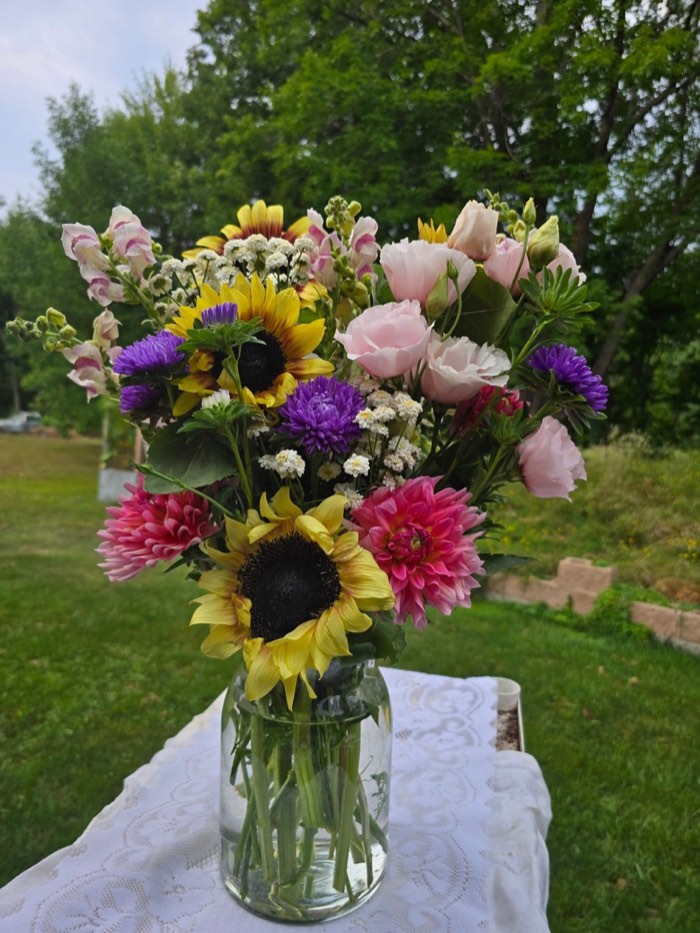 A bouquet of sunflowers, pink dahlias, purple asters and white yarrow in a glass jar, photographed outdoors